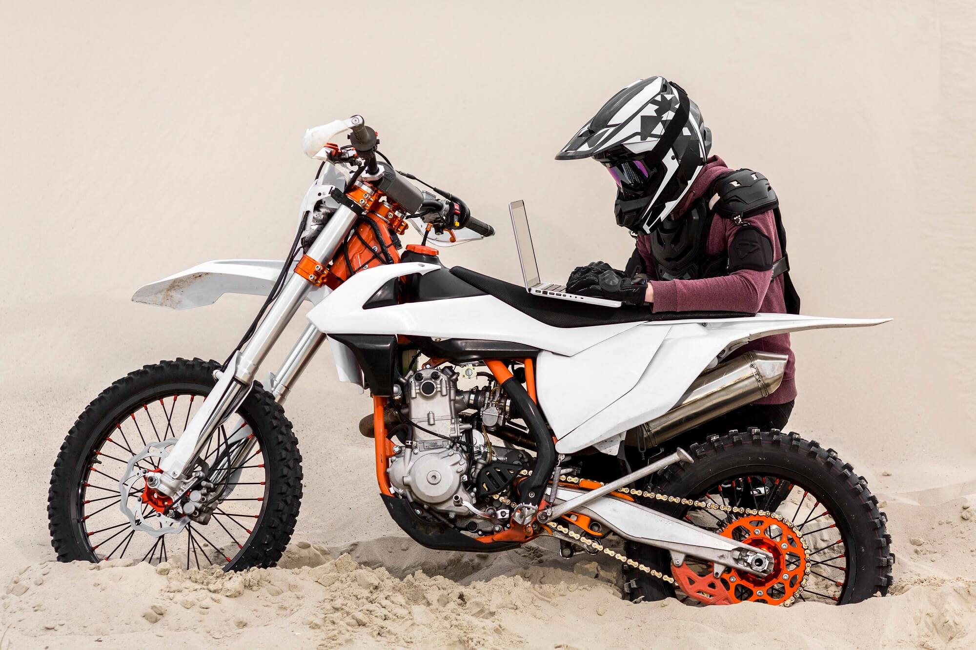Adventure motorcycle rider planning a Mongolia trip on a laptop in the desert
