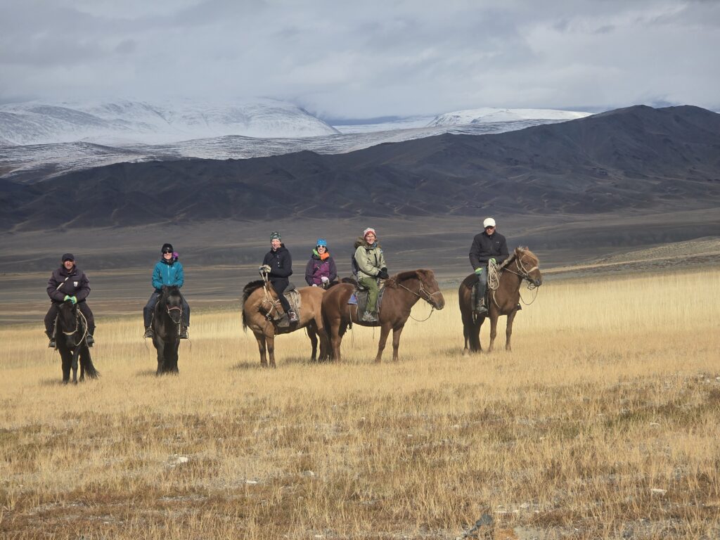 Tour group on horseback in autumn steppe below snow-dusted Altai peaks