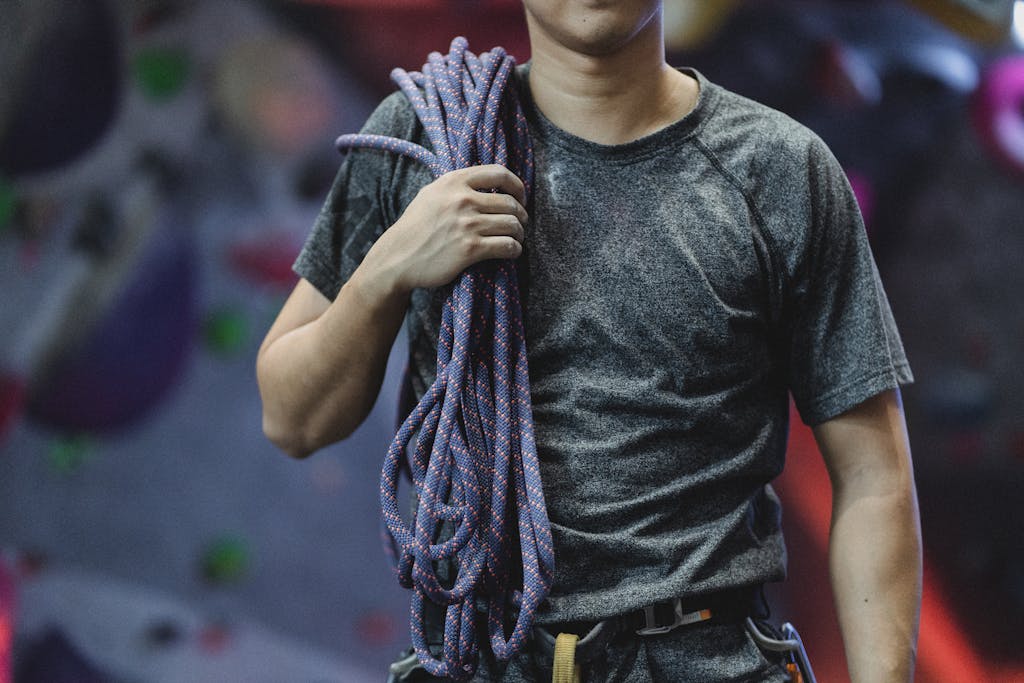 Crop unrecognizable male athlete in sportswear with belay and rope standing in bouldering center