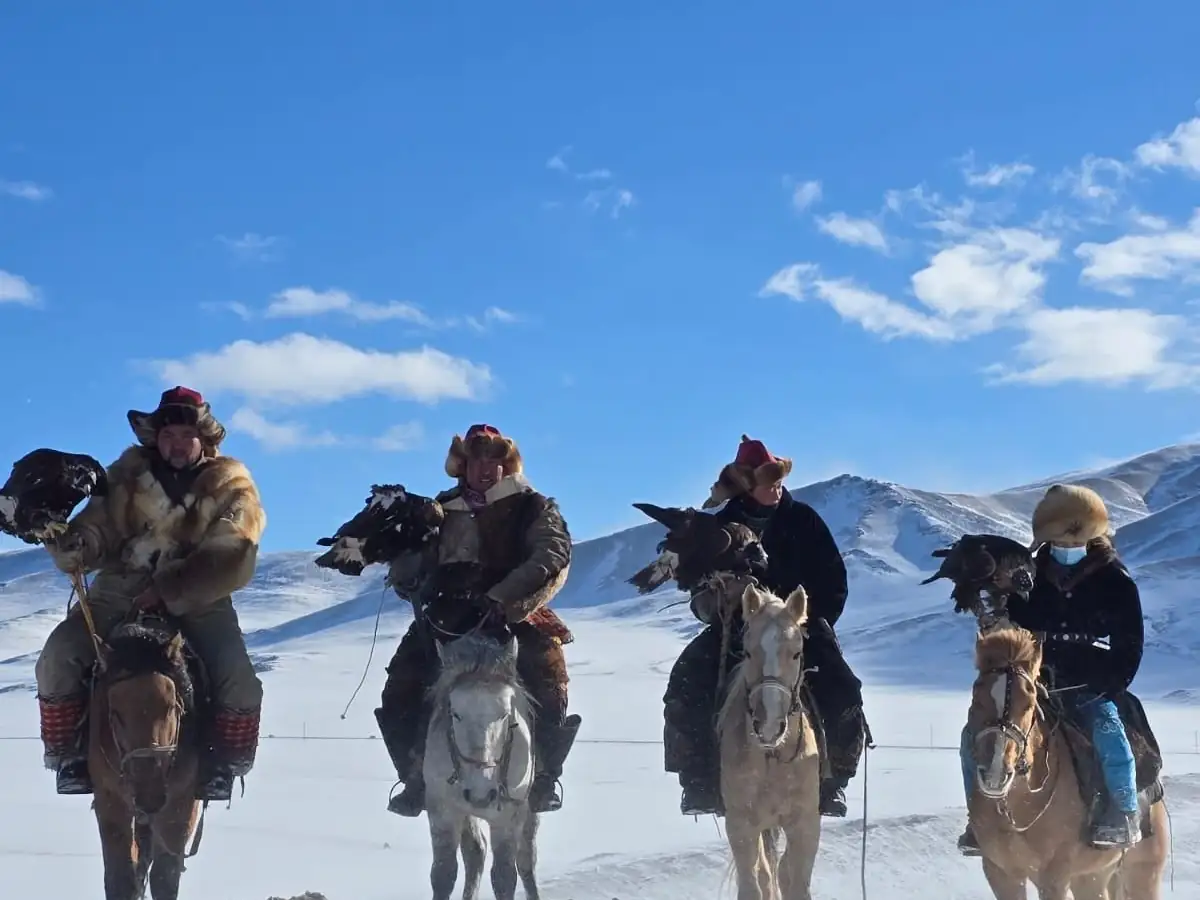 Eagle hunters riding in a line below snowy Altai mountains